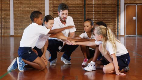 sports teacher and school kids stacking hands in basketball court