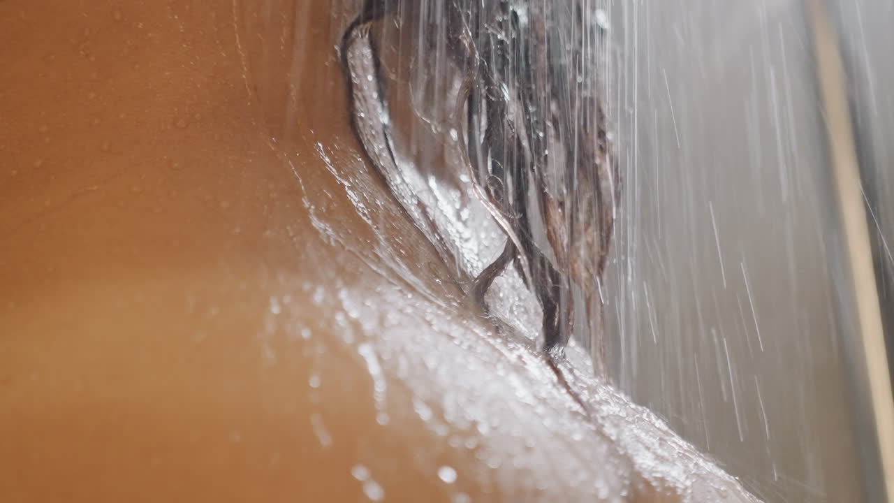 Spalla insaponata sotto la doccia dell'hotel, schiuma di sapone che ricopre la pelle, getto d'acqua che risciacqua la schiuma, primo piano tattile, atmosfera del bagno boutique, ospite che si lava i capelli, viaggiatore d'affari che si pulisce, atleta