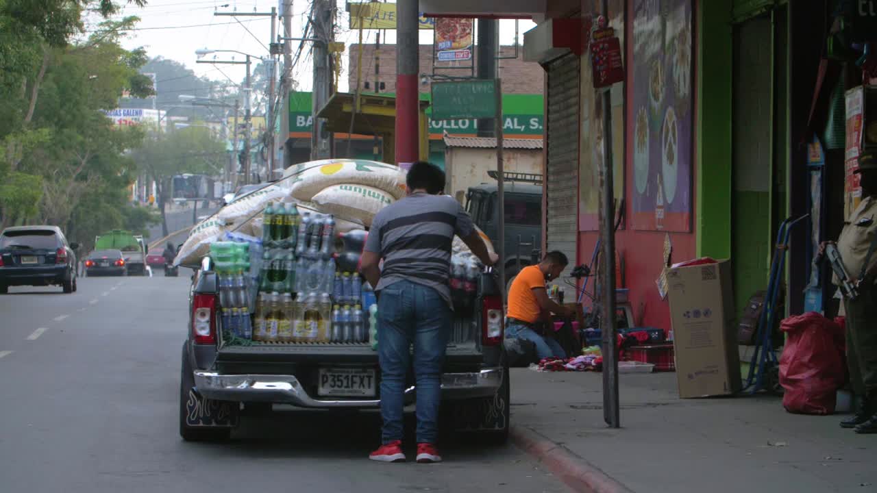Slow motion street view of overloaded vehicle unloading rice bags and soda bottles on side in Zone 18 Guatemala City - Handheld camera