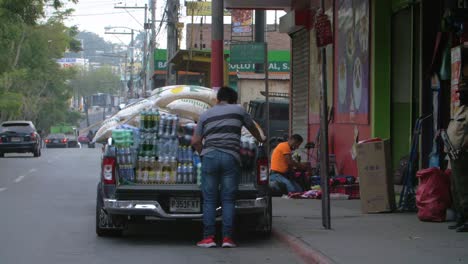 slow motion street view of overloaded vehicle unloading rice bags and soda bottles on side in zone 18 guatemala city - handheld camera