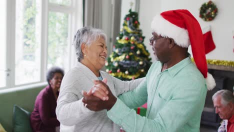 Glückliches,-Vielfältiges-älteres-Paar,-Das-Zur-Weihnachtszeit-Zusammen-Mit-Freunden-Im-Hintergrund-Tanzt