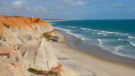 Vista-Aérea-De-La-Playa-De-Morro-Branco,-Desde-El-Acantilado-Hasta-El-Mar,-Ceará,-Brasil.