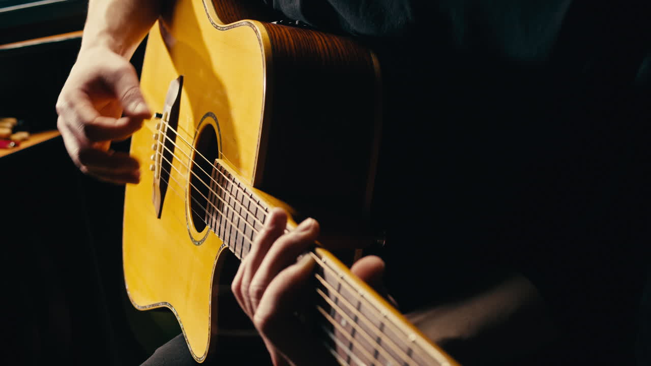 Giovane musicista che controlla le corde di una chitarra acustica, primo piano. Chitarrista uomo che accorda lo strumento musicale.
