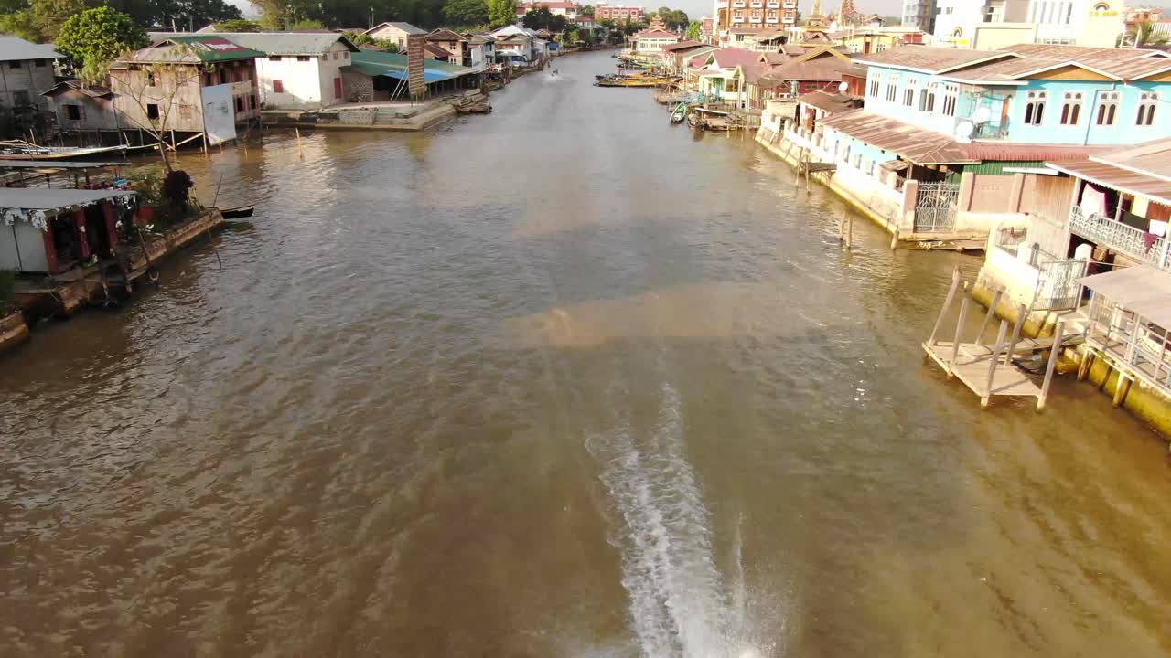 barco conduciendo por el río en nyaung shwe myanmar en el lago inle, edificios tradicionales en segundo plano