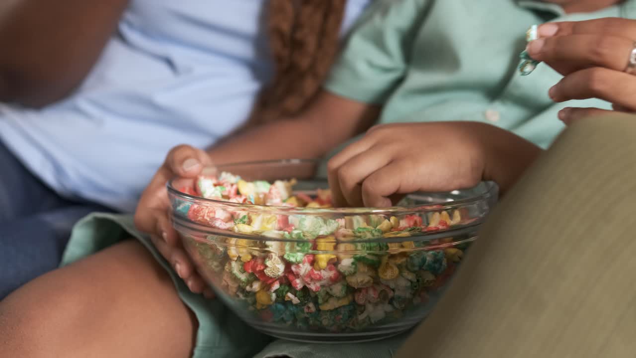 Close-up of hands reaching for colorful cereal or snack from a shared bowl