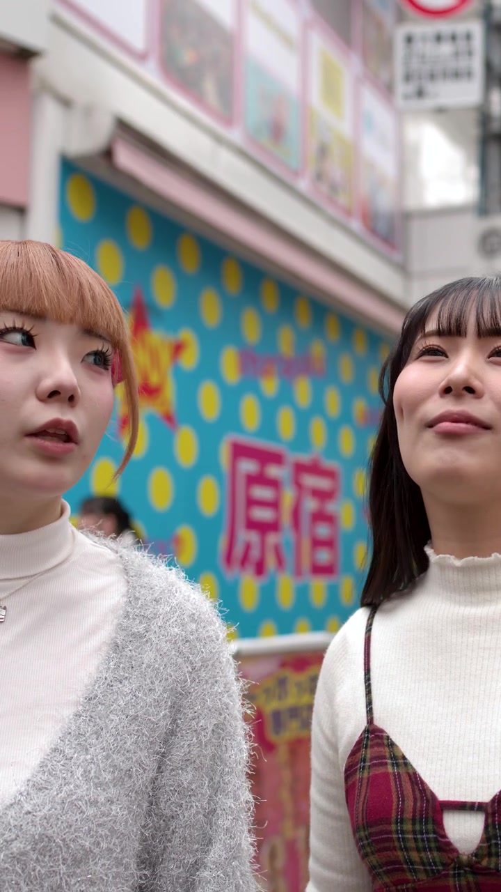 2人のスタイリッシュな若い女性が、賑やかな街路を歩きながら一緒に店のショーウィンドウを見上げている。