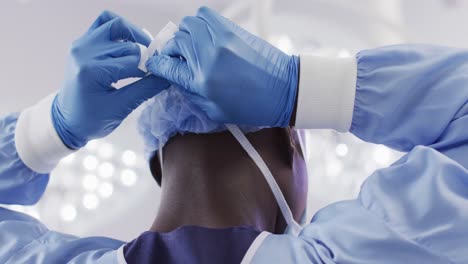 Back-view-of-african-american-male-surgeon-in-gloves-tying-face-mask-in-operating-theatre