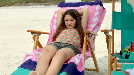 a little girl stares out at the ocean from her beach chair