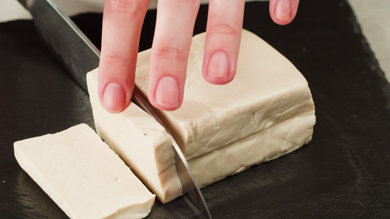 Fried tofu with sesame seeds and spices on cast iron pan, cooking japanese salad. Healthy ingredient for cooking vegan vegetarian diet food. Roasted tofu over black background.