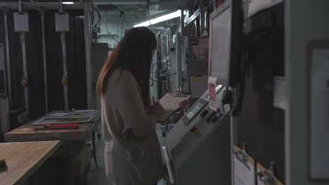 Medium-shot-of-a-woman-writing-on-paper-on-a-binder-inside-an-industrial-factory