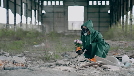 woman in safety uniform in abandoned place. scientist in protective suit and respirator with tendy flowers in ruined building. environment in danger.