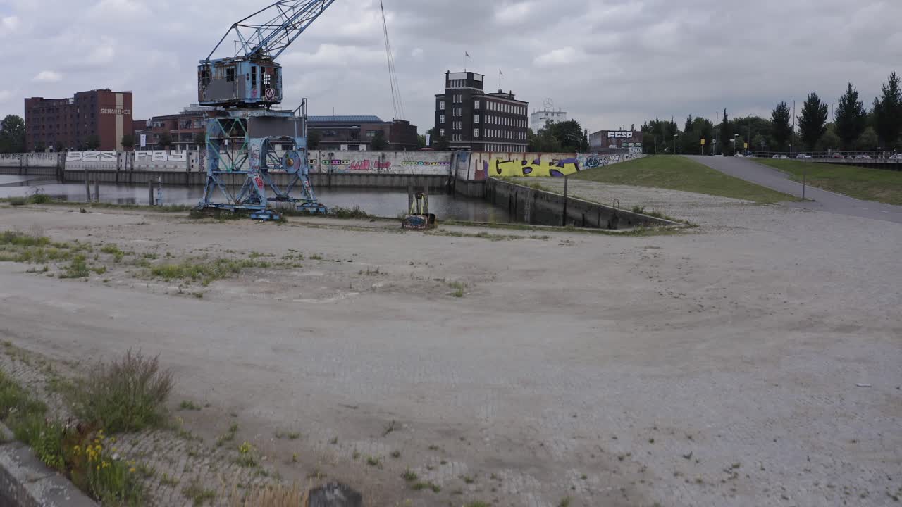 Drone view of weathered destroyed industrial crane placed near water of urban channel seen in cloudy summer day