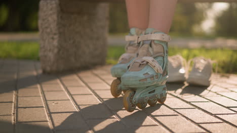 leg view of lady in roller skates moving back and forth on paved ground with sneakers slightly blurred behind, sunlight casting shadows, surrounded by greenery