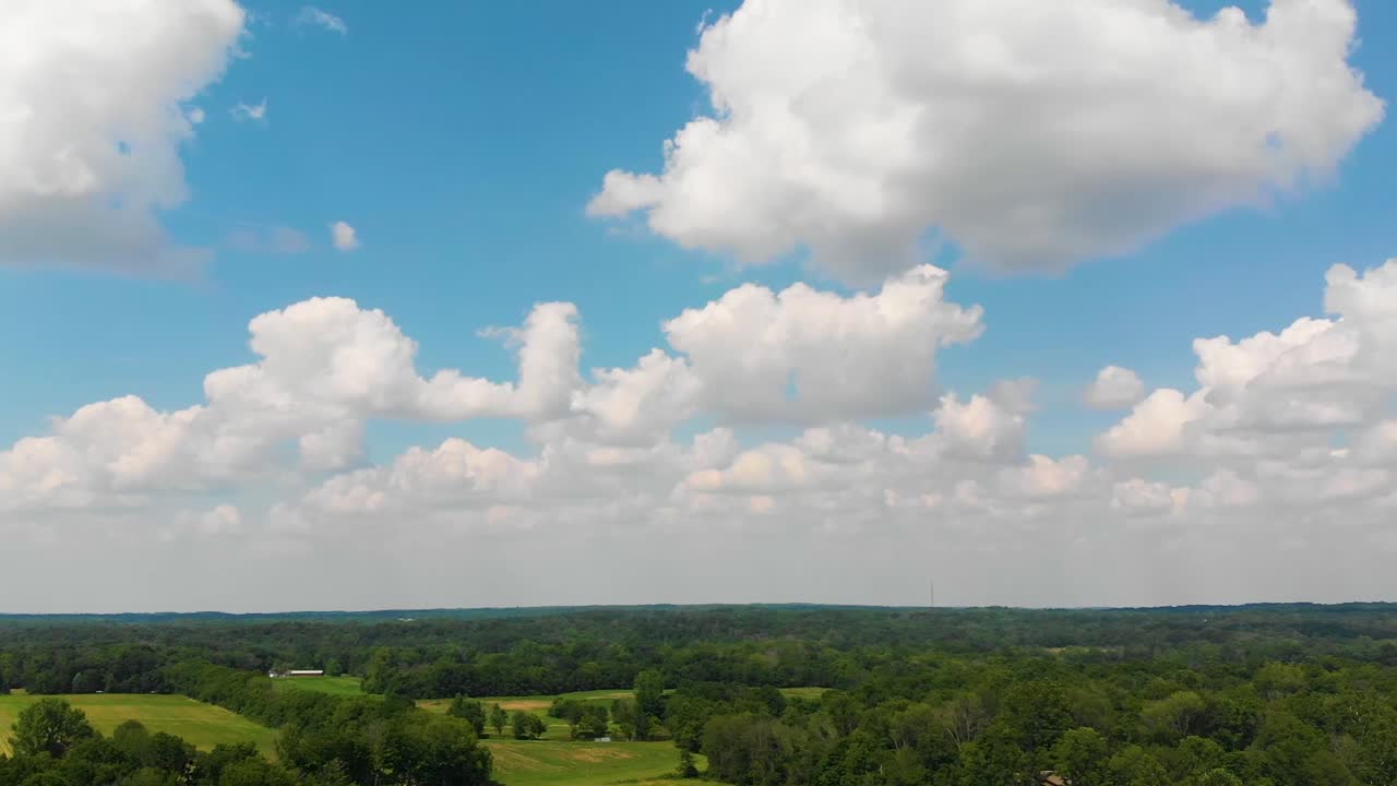 Fluffy white clouds over farmland and woodland.  Green