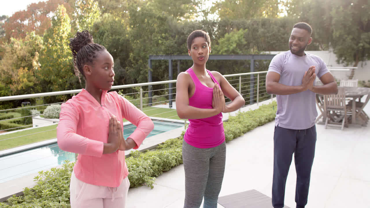felices padres afroamericanos y su hija practicando yoga en un jardín soleado, en cámara lenta.
