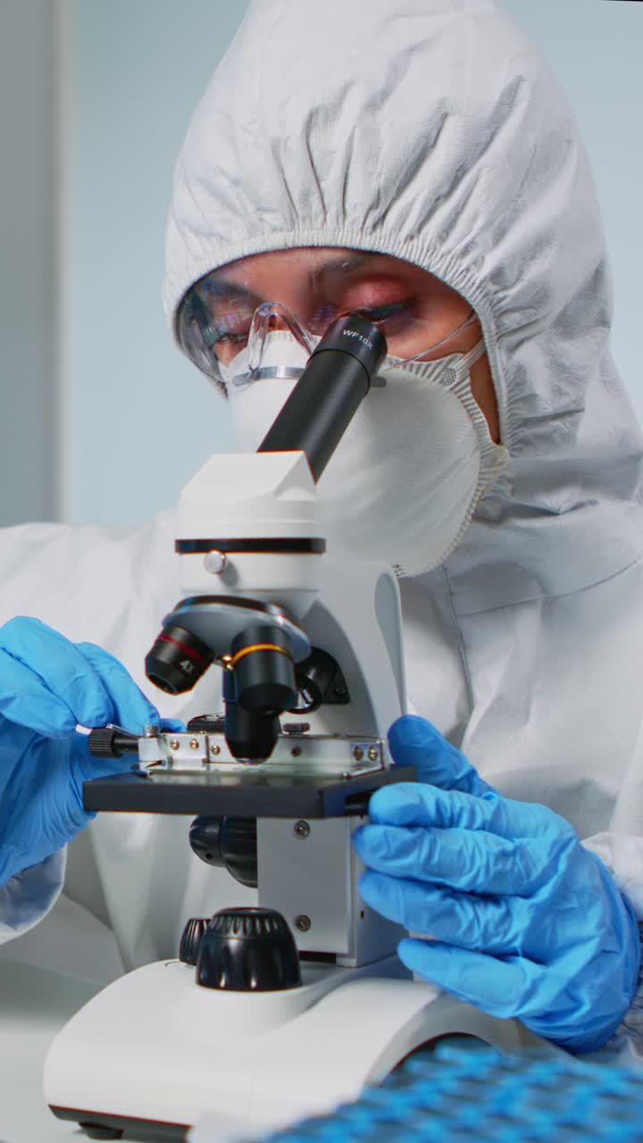 Vertical video: Scientist wearing ppe suit looking at samples under microscope