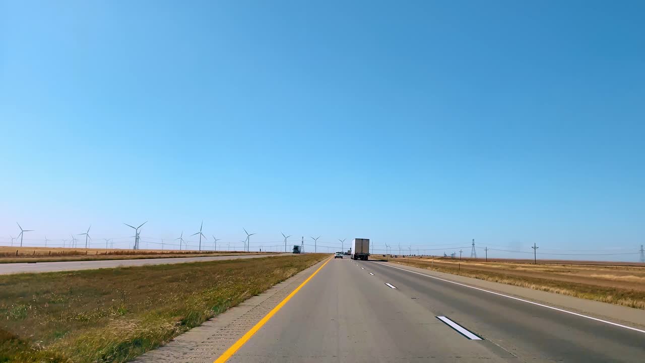 風力タービンが立ち並ぶ高速道路を走行するセミトラック。澄み切った青空の下、風力タービンと共に州間道路を走る商用車。