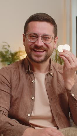 portrait of happy young male freelancer trader showing golden bitcoins sitting at home office table