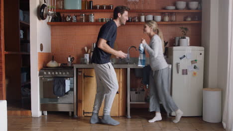 Feliz-Pareja-Joven-Bailando-En-La-Cocina-Disfrutando-De-Un-Divertido-Baile-Juntos-Divirtiéndose-Celebrando-La-Relación-El-Fin-De-Semana-En-Casa