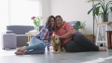 Portrait-of-caucasian-lesbian-couple-embracing-and-smiling-with-dog