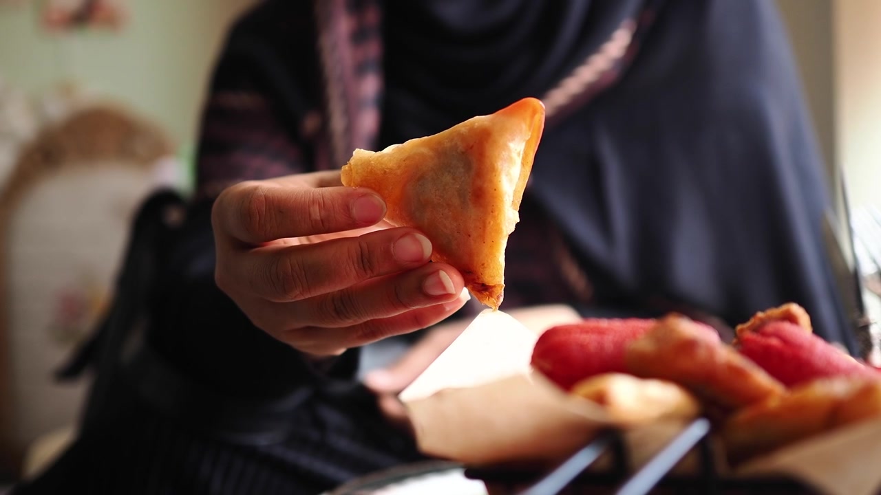 Primo piano di una mano che tiene uno snack samosa con ketchup.