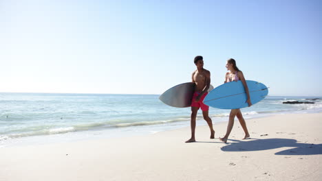 biracial man and caucasian woman carry surfboards on a sunny beach with copy space