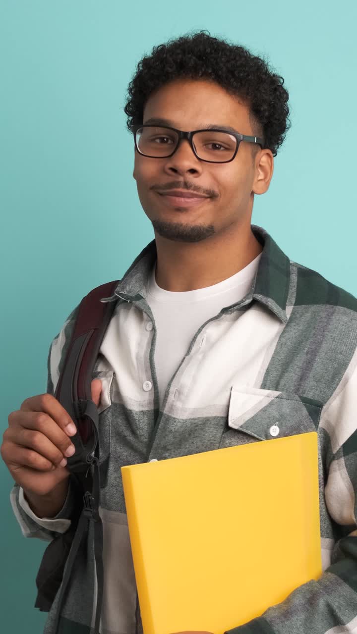 Happy male university student with backpack and books in blue studio