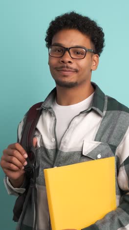 happy male university student with backpack and books in blue studio