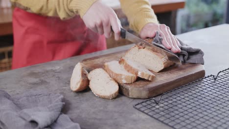 Hands-of-caucasian-man-cutting-bread-in-kitchen,-slow-motion