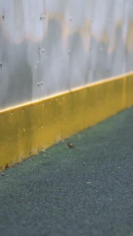 subtle reflection of a person visible on a metallic wall as a soccer ball hits the surface, with dynamic motion and impact captured under bright lighting in an urban sports setting