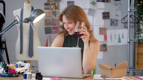 female owner of fashion business with glass of wine making video call on laptop in studio