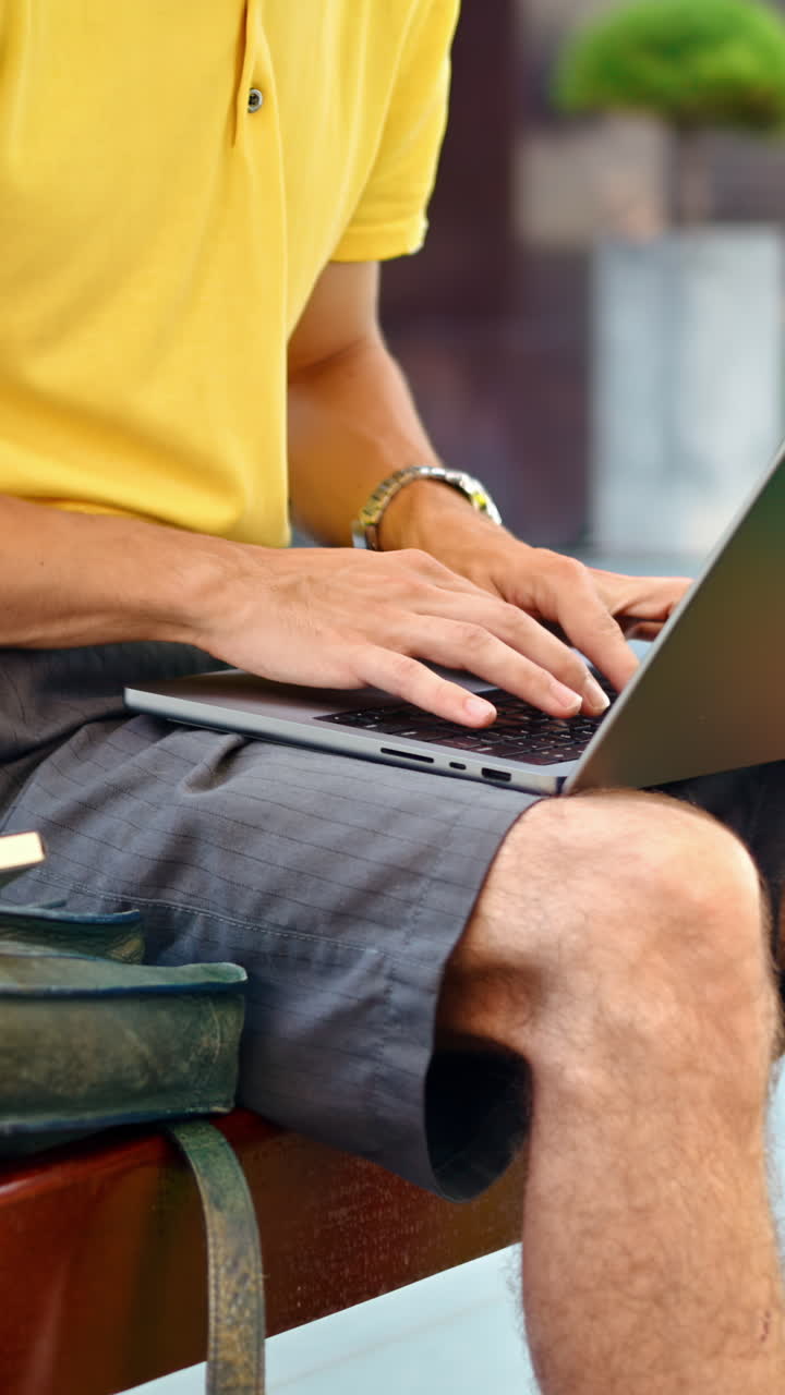 Man in yellow shirt talking standing on a bench and working on a laptop. Vertical