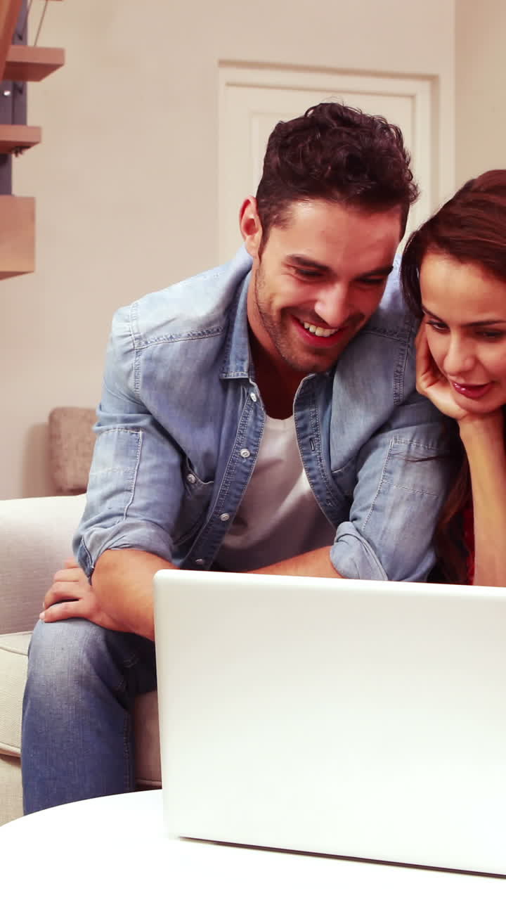 pareja feliz usando una computadora portátil en el sofá