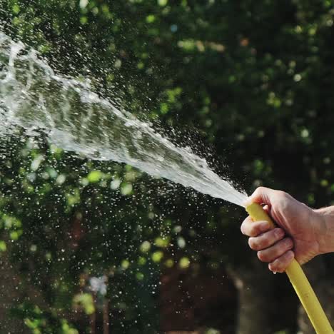 stream of water spraying from garden hose. male hand close-up. slow motion.
