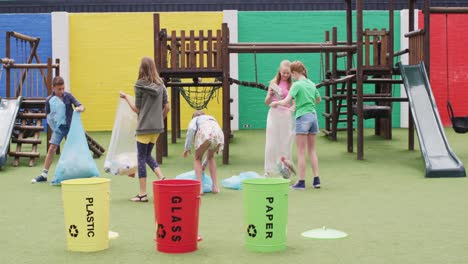 happy caucasian schoolchildren segregating waste together with bags at school playground