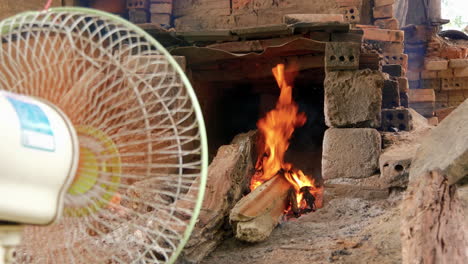 Wide-view-of-blazing-wood-fire-in-pottery-kiln,-fan-stokes-fire,-Than-Ha-Vietnam