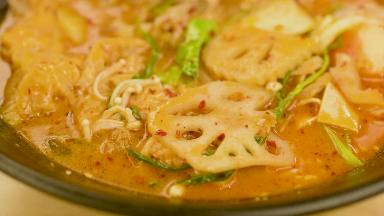 Close-up of hot spicy noodle soup with pork, fish ball, lotus root, vegetables, warm lighting