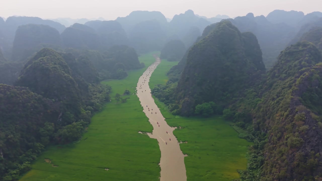 Cảnh quay drone điện ảnh nghiêng lên hé lộ dòng sông Tràng An với những chiếc thuyền du lịch đi qua các khối núi đá vôi hùng vĩ ở Ninh Bình, Việt Nam