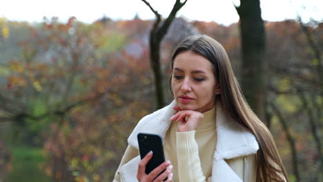 woman using a phone in a park during autumn