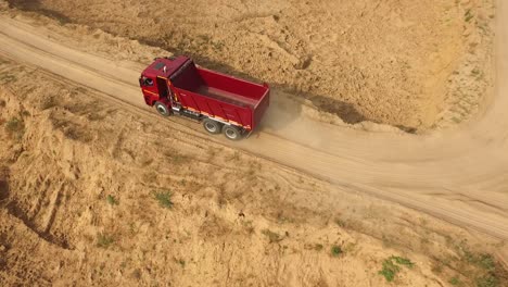 red dump truck driving on a dirt road in a quarry