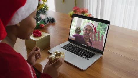 Afroamerikanische-Frau-Mit-Weihnachtsmütze-Nutzt-Laptop-Für-Weihnachtsvideoanruf-Mit-Mann-Auf-Dem-Bildschirm