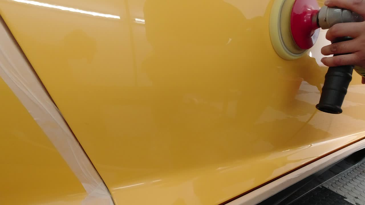 Yellow supercar's panel being polished with rotary machine