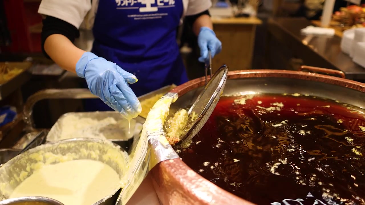 Uno chef che indossa guanti blu frigge tempura in una grande pentola di rame piena d'olio