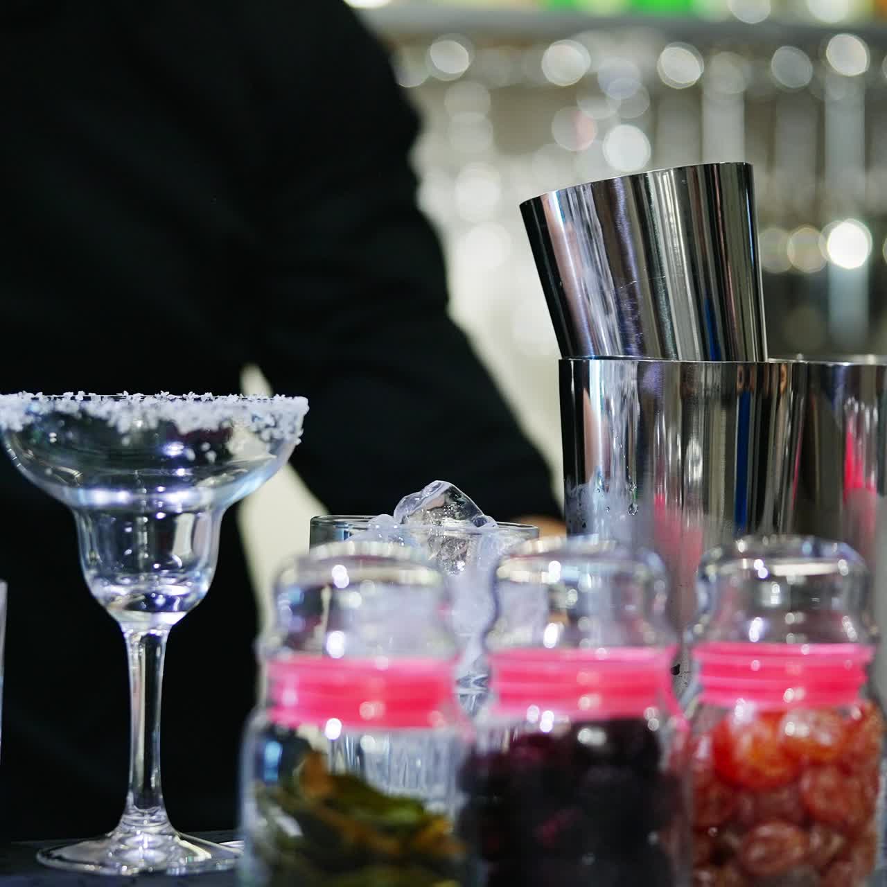 Male bartender wearing black shirt making cocktails. Professional using metal cups to mix the beverages