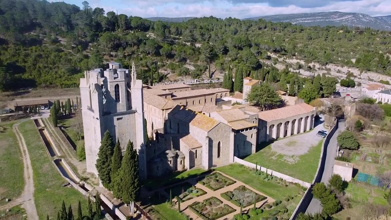Abbazia di Lagrasse (Abbaye Sainte-Marie de Lagrasse). Veduta aerea panoramica dei chiostri, della torre, dei giardini e degli orti monastici accanto a una collina boscosa. Monastero benedettino. Aude. Francia