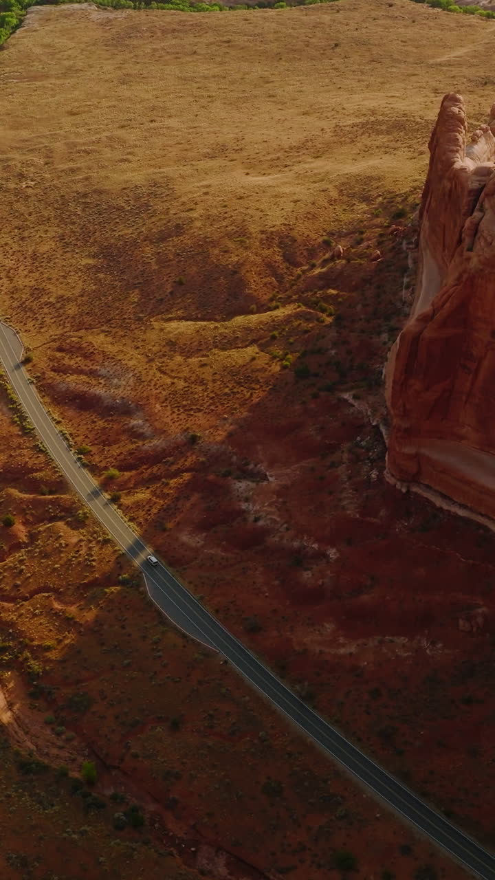 Big rocky canyon wall with rounded smooth stones and tops. Highway crossing the desert landscape with some cars moving on. Aerial perspective. Vertical video