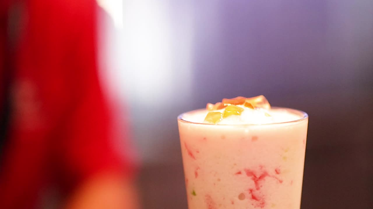 Metal bir kaşık, bir bardaktaki kalın pembe smoothie'nin üzerine renkli jöleli malzemeler döküyor.