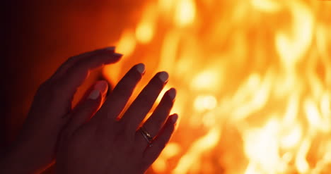 woman warms hands by the fireplace at home