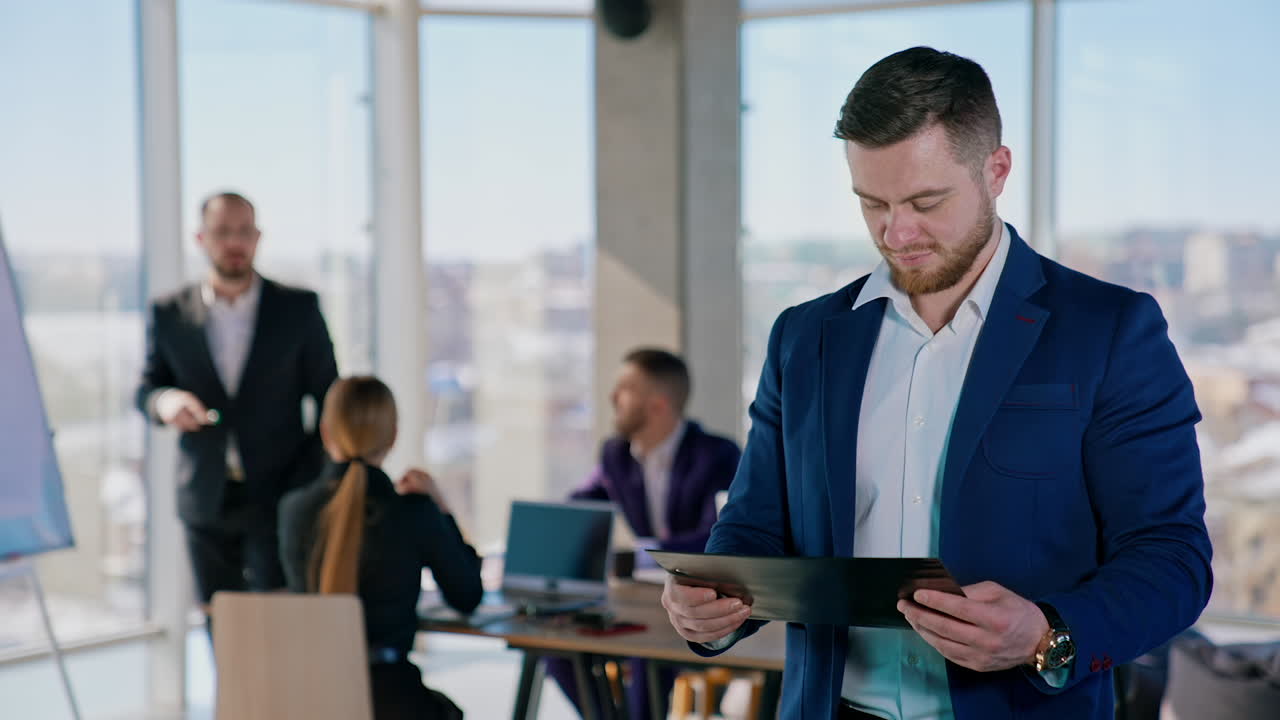 Young businessman with papers in office center. Portrait of a handsome bearded entrepreneur in white shirt and suit holds a folder and reading documents.