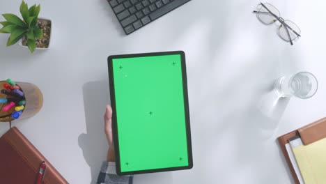 vista de arriba hacia abajo de una computadora portátil con pantalla verde simulada pantalla chromakey en un escritorio de oficina de madera al lado de la libreta con bolígrafos, gafas y un vaso de agua.